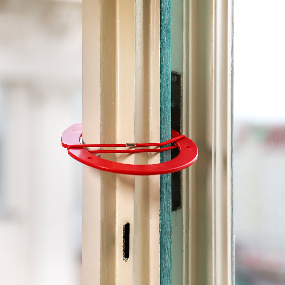 Rote Lüftungsklammer für Kastenfenster an geöffnetem Fensterrahmen zur sicheren Belüftung